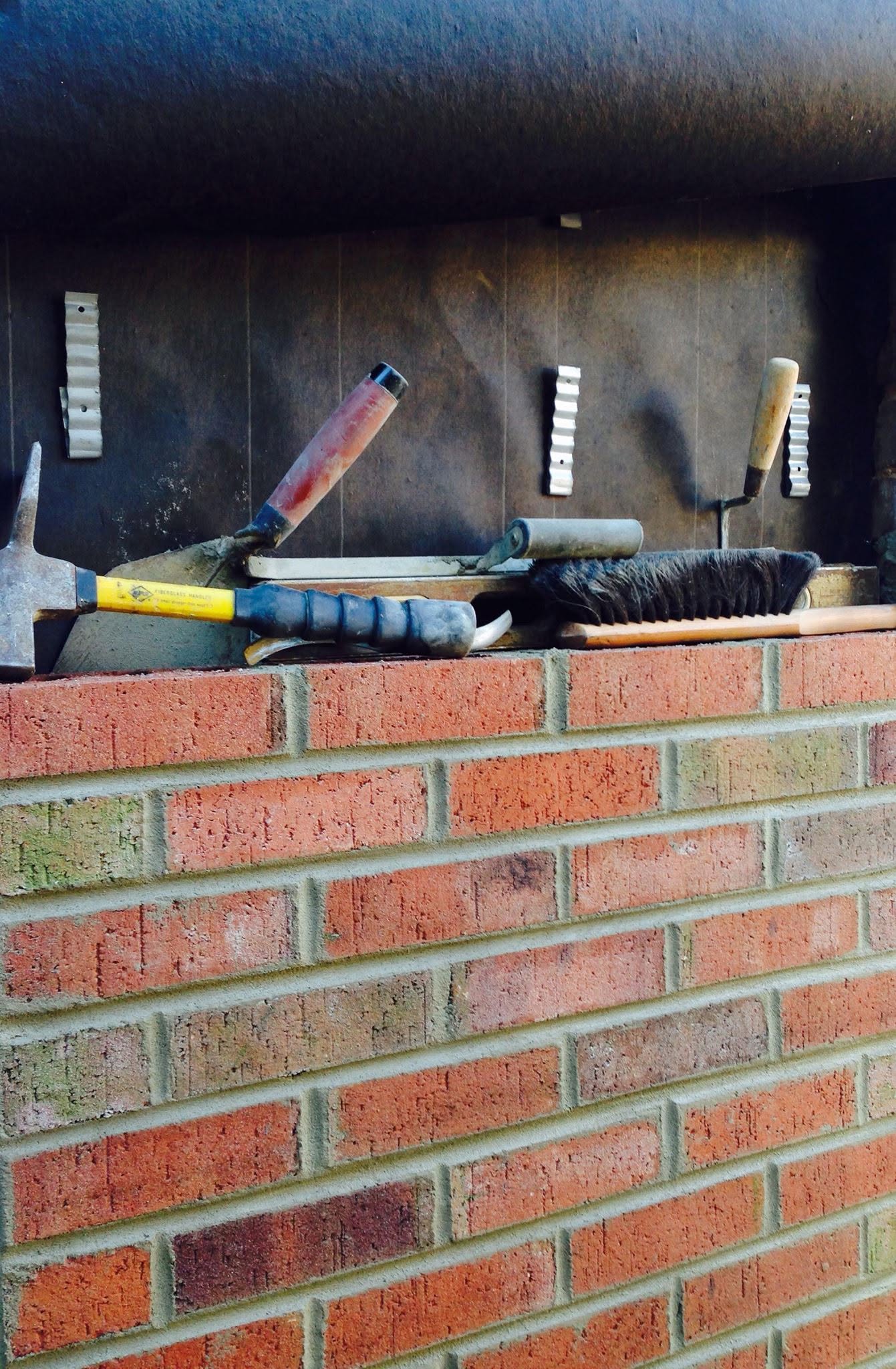 Brick wall under construction with a mason's tools laid out beside it