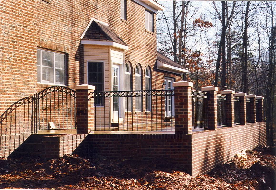 Brick and stone entry columns with an iron fence at a residential entrance